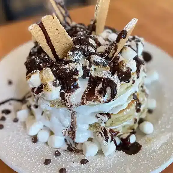 Chocolate chip pancakes stacked with whipped cream and syrup